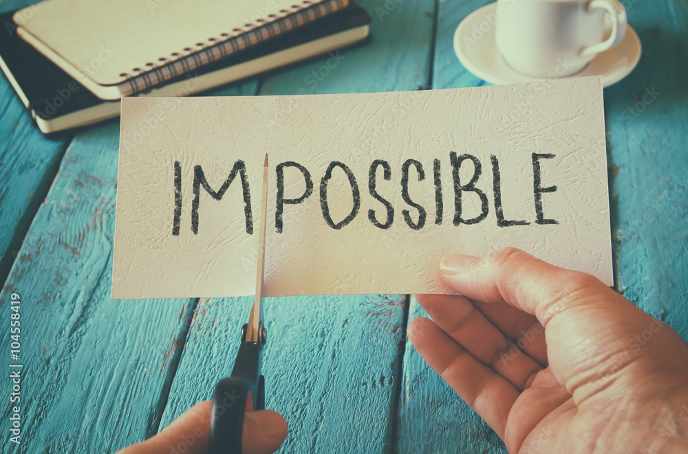 Aufkleber man hand holding card with the text impossible, cutting the word im so it written possible. success 