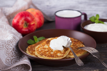 Cottage cheese pancake with apples in ceramic bowl with sour cream and a glass of milk on a dark wooden table