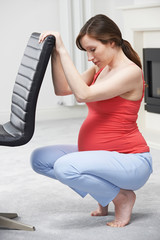 Pregnant Woman Exercsing Using Back Of Chair At Home
