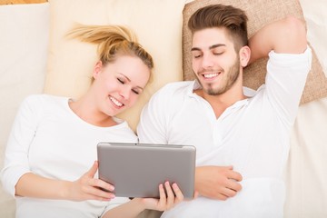 A young and happy couple with a tablet PC  in bed from above..