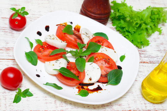 Caprese salad. Italian cuisine. Mediterranean cuisine. Tomatoes, mozzarella, basil leaves and olive oil on wooden table. 