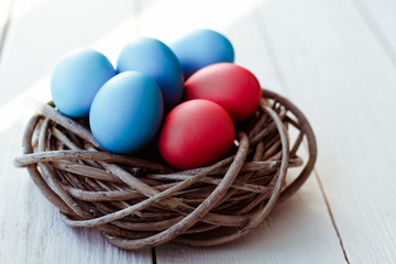 Multicolored Easter eggs in wicker basket on white wooden background