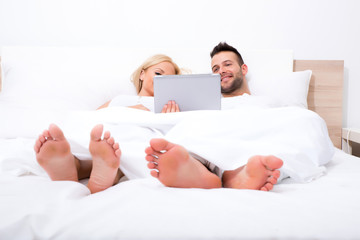 Beautiful young couple using a Tablet PC in Bed.