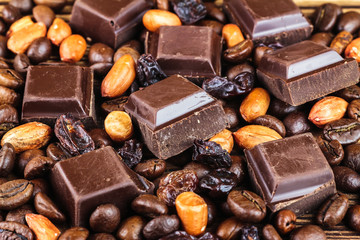 Dark chocolate cubes, coffee beans, peanuts and raisins, close-up