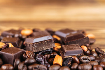 Dark chocolate cubes, coffee beans, peanuts and raisins on wooden table, close-up