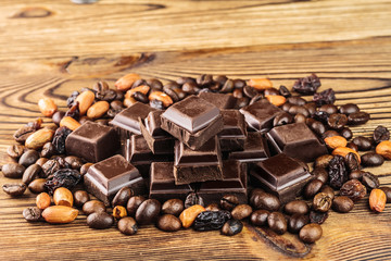 Dark chocolate cubes, coffee beans, peanuts and raisins on wooden table, close-up