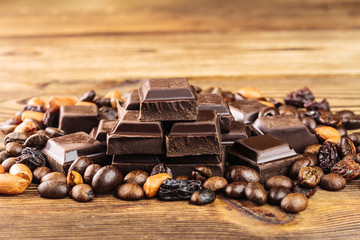 Dark chocolate cubes, coffee beans, peanuts and raisins on wooden table, close-up