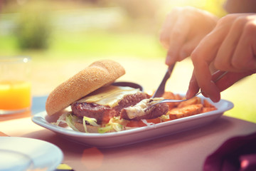 Man eating burger with fries and orange juice on summer terrace