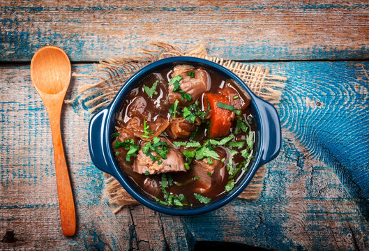 Meat stew with vegetables and herbs on old wooden table