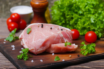 Sliced pieces of raw meat for barbecue with fresh Vegetables (tomatoes, lettuce) on wooden surface. Meat raw stacked on wooden background, beef Steak BBQ. 