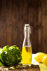 Olive oil in a glass bottle, lemon, lettuce on a wooden background