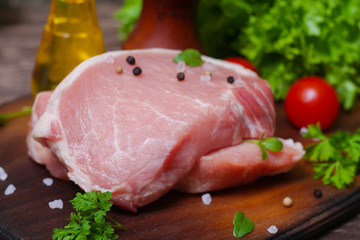 Sliced pieces of raw meat for barbecue with fresh Vegetables (tomatoes, lettuce) on wooden surface. Meat raw stacked on wooden background, beef Steak BBQ. 