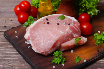 Sliced pieces of raw meat for barbecue with fresh Vegetables (tomatoes, lettuce) on wooden surface. Meat raw stacked on wooden background, beef Steak BBQ. 