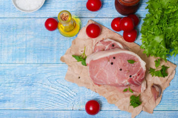 Sliced pieces of raw meat for barbecue with fresh Vegetables (tomatoes, lettuce) on wooden surface. Meat raw stacked on wooden background, beef Steak BBQ. 