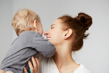 Young mother with her one years old little son dressed in pajamas are relaxing and playing in the bedroom at the weekend together, lazy morning, warm and cozy scene. Selective focus.