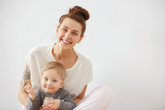 Young Attractive Mother With Her One Years Old Little Son Dressed In Pajamas.  Boy Eating A Fruit Smoothie Himself In The Bedroom At The Weekend Together, Warm And Cozy Scene. Selective Focus.