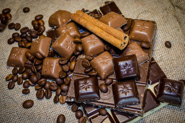 chocolate bar, coffee beans and cinnamon sticks on a sack background