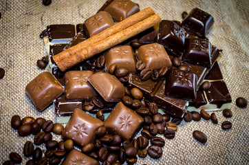 chocolate bar, coffee beans and cinnamon sticks on a sack background