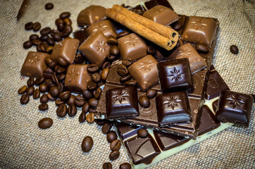 chocolate bar, coffee beans and cinnamon sticks on a sack background