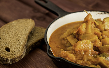 Vegetable Ratatouille in antique iron frying pan on a wooden table with two pieces of rye bread