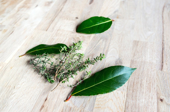 fresh branch of thyme and leaf of fresh bay laurel on an oak tree cutting board 