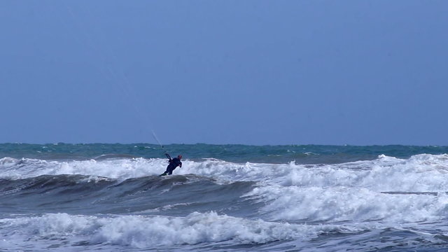 A kitesurfer is surfing in big waves in a windy, sunny and solitary beach