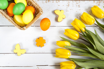 Easter eggs, homemade cookies and yellow tulips over light background with copy space