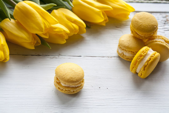 Yellow lemmon macaroons and yellow fresh tulips  on light wooden background 