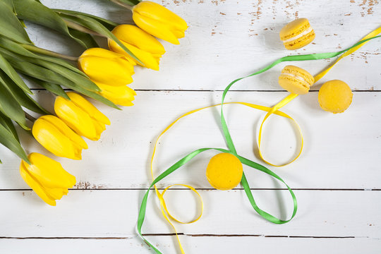 Yellow lemmon macaroons and yellow fresh tulips  on light wooden background 
