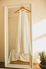white wedding dress on a hanger hanging on mirror