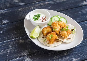 Crispy fried fish on a homemade tortilla on a dark wooden background