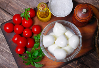 Italian cuisine. Mediterranean cuisine.  Traditional italian mozzarella cheese in glass bowl with basil, tomatoes and olive oil - caprese salad ingredients, on rustic wooden background. Rustic style