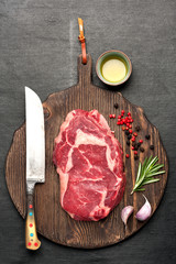 Ribeye steak and spices on a wooden board prepared for roasting.  top view