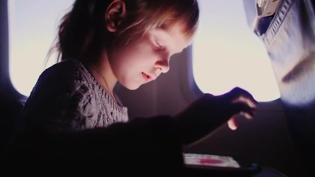 little girl is drawing on a tablet in an aircraft