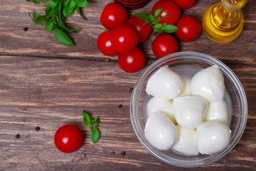 Italian cuisine. Mediterranean cuisine.  Traditional italian mozzarella cheese in glass bowl with basil, tomatoes and olive oil - caprese salad ingredients, on rustic wooden background. Rustic style