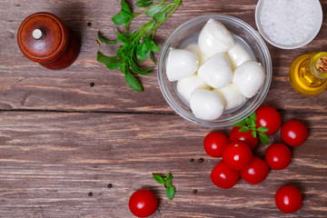 Italian cuisine. Mediterranean cuisine.  Traditional italian mozzarella cheese in glass bowl with basil, tomatoes and olive oil - caprese salad ingredients, on rustic wooden background. Rustic style