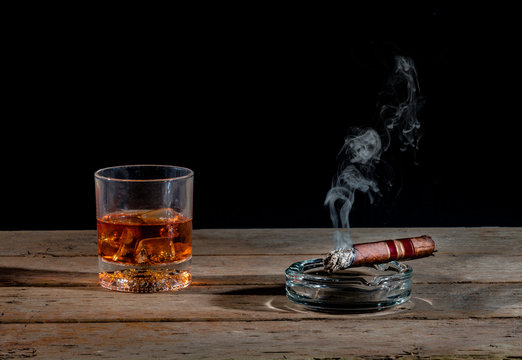 Glass of whiskey and lit cigar on rustic tabletop