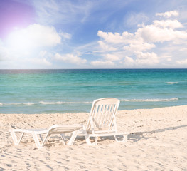 White plastic chairs on white sand beach with sun flare effect