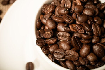 Cup, saucer and coffee beans on a burlap background. Shallow dep
