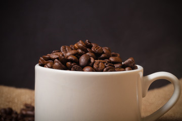 Cup, saucer and coffee beans on a burlap background. Shallow dep