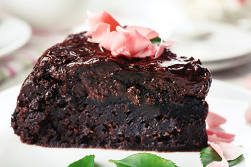 Piece of chocolate cake decorated with flowers on white wooden table