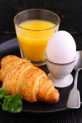 Weekend breakfast: croissants, boiled egg and orange juice, black background