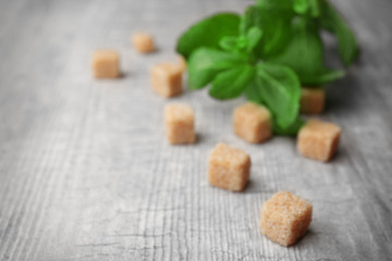 Fototapeta na wymiar Pile of brown sugar cubes and stevia on grey wooden background