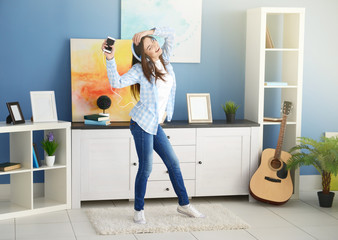 Happy young woman with headphones dancing and listening to music at home