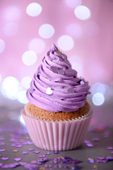 Cupcake with purple cream icing on a glitter background, close up