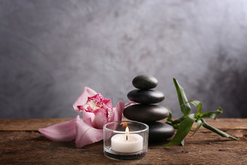 Spa stones with bamboo, pink orchid and candle on wooden table against grey background