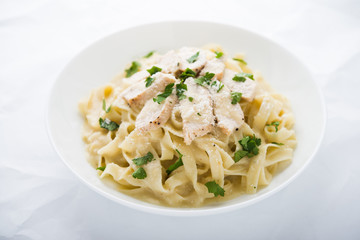 Pasta fettuccine alfredo with chicken, parmesan and parsley on white background close up. Italian cuisine.