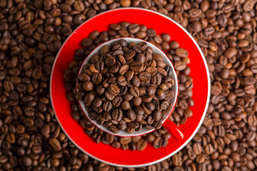 A red cup of coffee bean on the coffee beans background. Top view