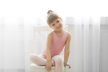 Little cute girl in pink leotard sitting on chair at dance studio