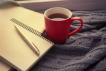 Red cup of tea, book  and warm knitted plaid on windowsill, close up